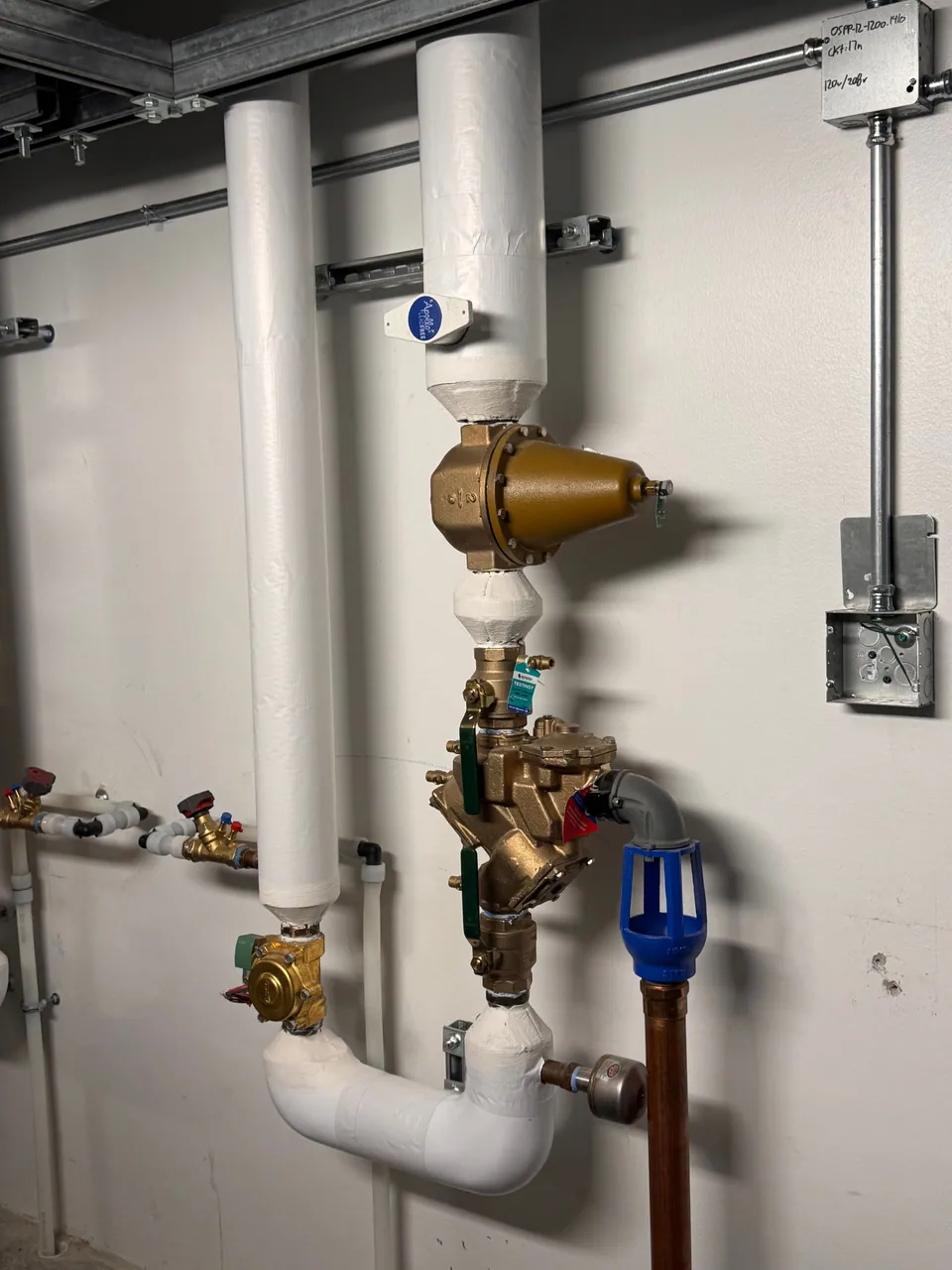 Brass pressure-reducing valve and backflow preventer on an insulated water riser in a mechanical room