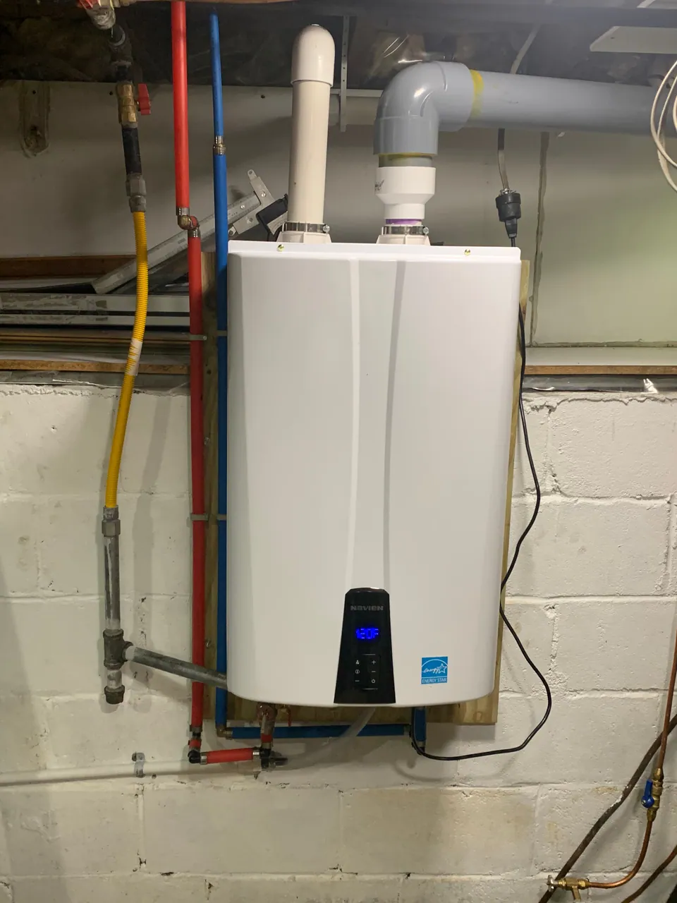Wall-mounted tankless water heater with new gas, water and vent piping on a block wall