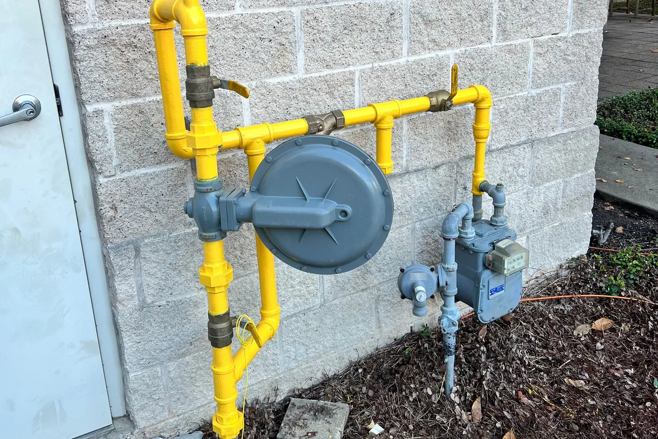 New yellow-painted gas piping with a gray regulator and meter on a block wall outside a building